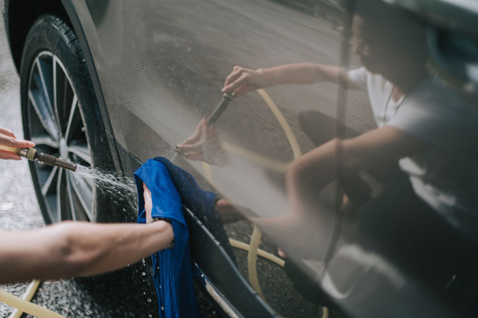 an asian chinese teenager boy washing and cleaning car in front of his house